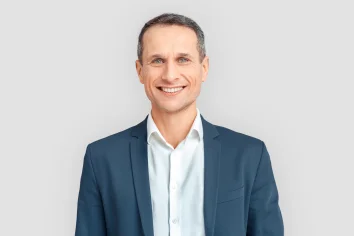 Ein seriöser Mann im Anzug lächelt freundlich und schaut Dich dabei an.